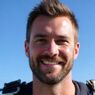Portrait of Mark Thompson, a confident male skydiving instructor with a clear blue sky in the background.