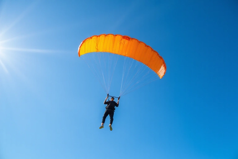 A person skydiving with a parachute open against a clear blue sky, illustrating freedom and adventure.